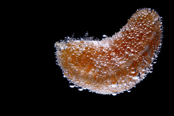 Mandarin slice in sparkling water isolated on black background