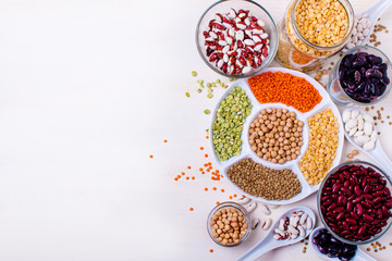 Different beans in bowls on a white wooden table, top view