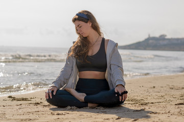 beautiful woman doing yoga and meditating on the seashore