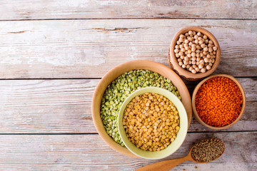 Different beans in bowls on a white wooden table, top view