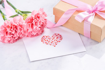 May mothers day handmade giftbox idea concept, beautiful blooming carnations with baby pink ribbon bow gift isolated on modern marble desk, close up, copy space, mock up