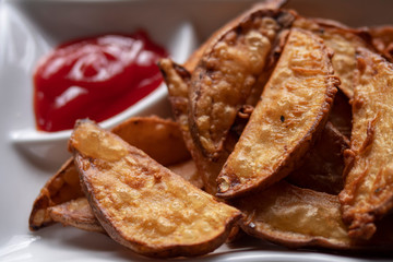 A plate with fried golden potatoes in country style with tomato sauce