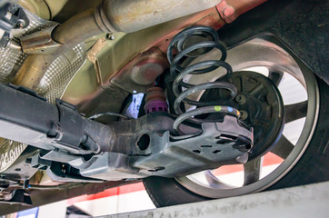 Closeup view of the rear suspension, rear brake and exhaust of a car seen from beneath in a inspection workshop