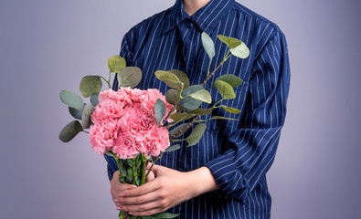 Young girl in dark blue striped shirt giving bunch of handmade beautiful blooming baby pink color carnations as a gift for mothers day concept, close up, copy space, clipping path