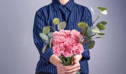 Young girl in dark blue striped shirt giving bunch of handmade beautiful blooming baby pink color carnations as a gift for mothers day concept, close up, copy space, clipping path