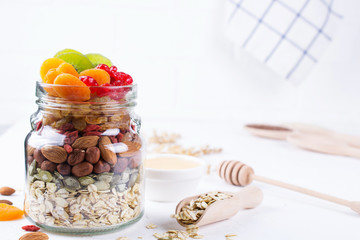 Glass jar with ingredients for cooking granola on white background. Oat flakes, honey, nuts, dried fruit and seeds. Healthy snak
