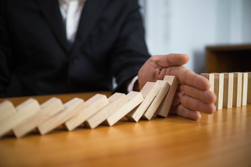 Businessman hand stops domino continuous overturned meaning that hindered business failure. Stop...