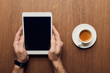 cropped view of man holding digital tablet with blank screen near cup of coffee