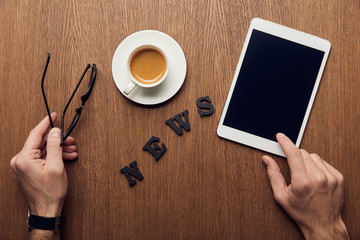cropped view of man holding digital tablet with blank screen and glasses near news lettering and cup of coffee