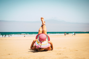 Beautiful lady enjoy the summer vacation at the beach lay down with up legs and pink hat for the sun - sunbathing activity and cute lifestyle  on the sand - people enjoy freedom from work