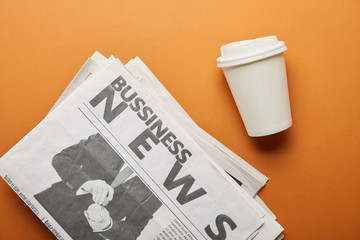 top view of business newspaper near paper cup with drink on orange