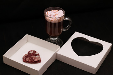 hot drink in a glass cup with pink marshmallows and white box with a transparent cover in the form of heart with cookies
