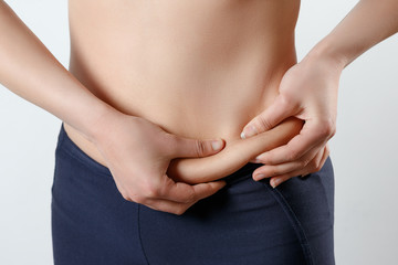 a young woman feels with two hands folds on her stomach. On light white background. Concept of weight loss, proper nutrition, excess weight, women's health