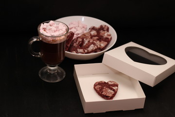 hot drink in a glass cup with pink marshmallows and white box with a transparent cover in the form of heart with cookies