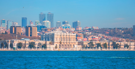 Fototapeta na wymiar Dolmabahce Palace (Dolmabahce Sarayi) seen from the Bosphorus - Dolmabahce palace against coastal cityscape with modern buildings under cloudy sky istanbul city 
