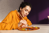 Smiling artistic woman choosing paint color on a palette