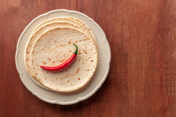 A red hot chilli pepper, shot from above on a pile of tortillas, Mexican flatbreads, on a dark rustic wooden background with copy space