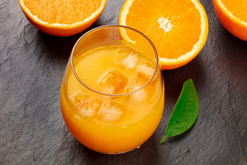 A glass of fresh orange juice with orange halves and a green leaf on a black background