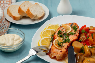 Baked salmon fillet medallion with salad of pickled vegetables and mushrooms on a white plate on a blue background