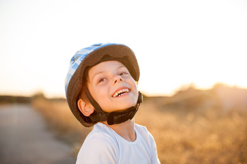 happy smiling little caucasian kid in helmet and white shirt outdoors leisure sport on warm sunset with copy space