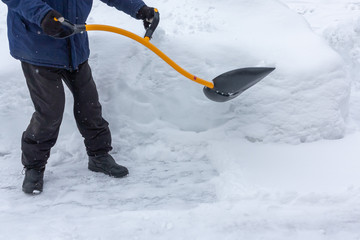 A man cleans snow in the yard with a shovel after a heavy snowfall