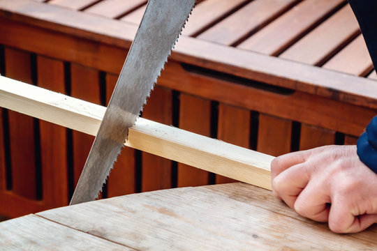 Men's hands sawing a wooden bar with a hacksaw