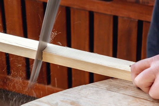 Men's hands sawing a wooden bar with a hacksaw