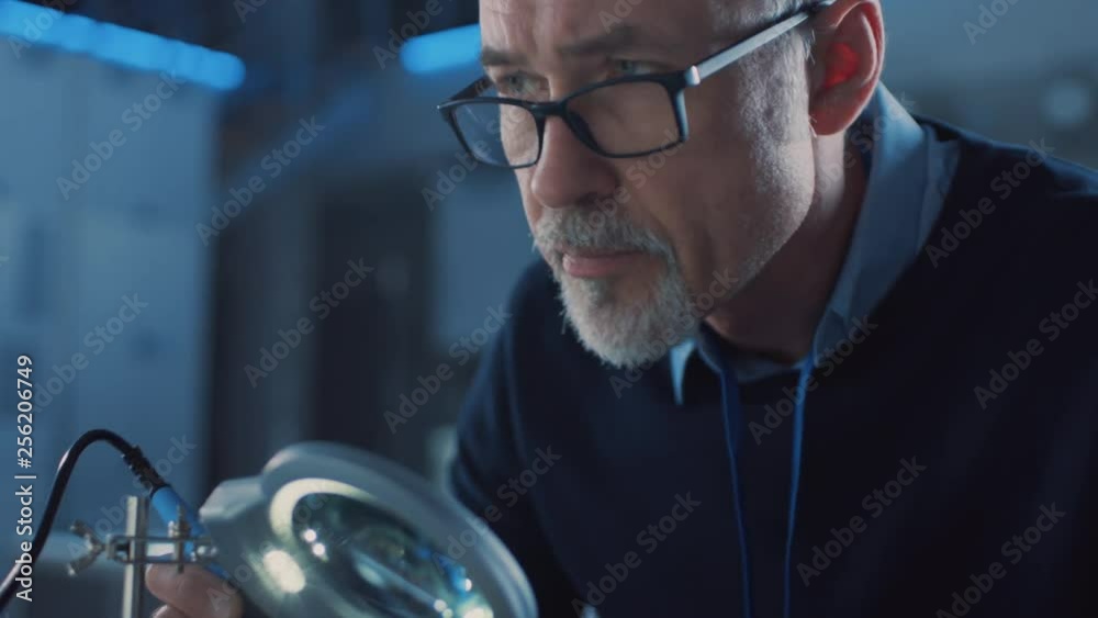 Poster electronics maintenance engineer enters his workshop with coffee beginss soldering of circuit board,