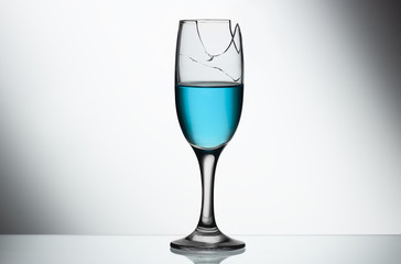 Broken champagne glass with blue liquid on a light background.