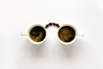 Human face with glasses from two espresso cups and coffee beans. Coffee art or creative concept. Top view