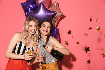 Photo of two young women 20s in stylish outfit holding festive balloons and drinking champagne on party