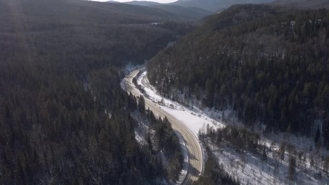 One yellow school bus driving on winding smooth snowy wild freeway in mountains forest - Aerial drone view