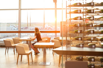 Woman waiting in the cafe in airport terminal and looking at window at airplane