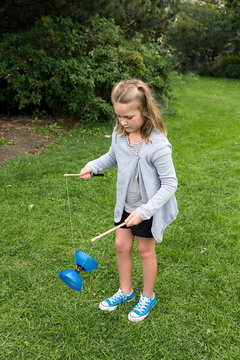 Pretty serious little girl in summer clothes standing outside in three-quarter profile juggling a diabolo in a park