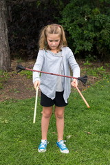 Pretty serious little girl in summer clothes standing outside juggling with devil sticks in a park