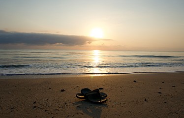 Obraz premium Shoes slippers flip-flops on the beach. Shoes on the sand by the sea on holiday. Shoes with sunrise background 