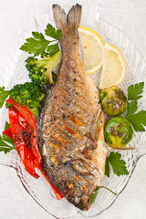 Grilled dorade fish  with vegetables, herbs and lemon on a dish