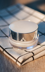 White lotion jar Lotion jars with seeds and flowers around The lotion bottle is placed on the wood.