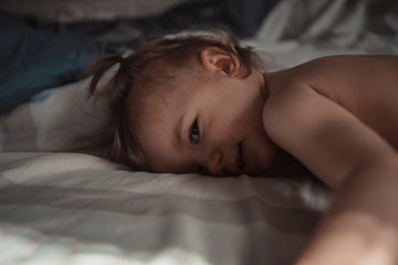 child with tails on his head favors morning in bed in his parents' room on a sunny day. concept of a family of typical, ordinary home-like recreation of a real middle-income family in Europe