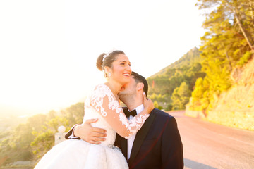 Beautiful wedding couple kissing in the sun near road and trees