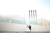 Handsome groom holds bride's hands posing in the front of glass building
