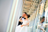 Handsome groom holds bride's hands posing in the front of glass building