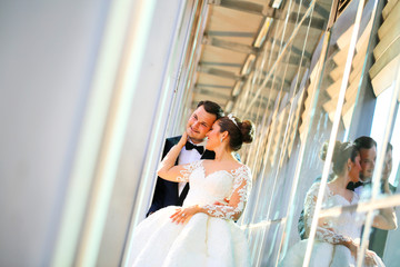 Handsome groom holds bride's hands posing in the front of glass building