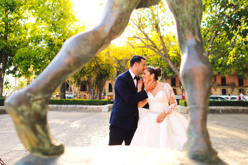 Groom kiss the bride in park near statue