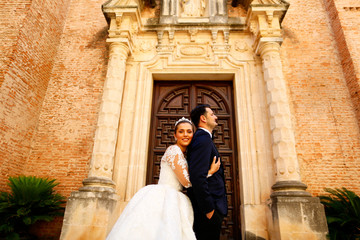 Fototapeta premium Beautiful bride embracing groom in front of old building