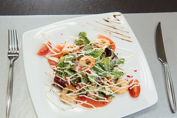 Salad with shrimps, salmon slices, tomatoes, greens on a plate on the table