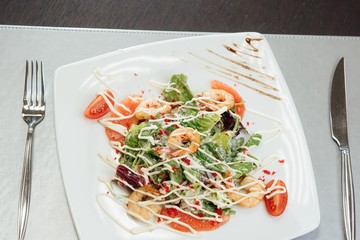 Salad with shrimps, salmon slices, tomatoes, greens on a plate on the table