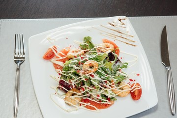 Salad with shrimps, salmon slices, tomatoes, greens on a plate on the table