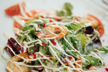 Salad with shrimps, salmon slices, tomatoes, greens on a plate on the table