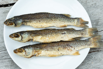 Deep fried fish In a white plate on a wooden table.